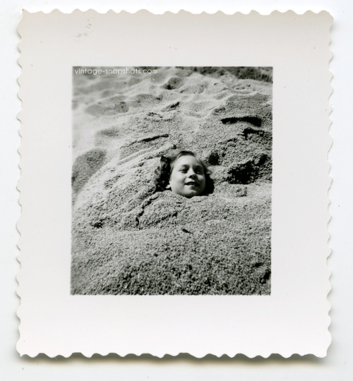 Vintage snapshot photo of girl buried in sand at the beach
